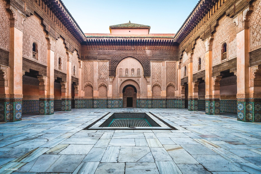 Interior courtyard of the Ben Youssef Madrasa in Marrakech with intricate stucco carvings, zellige tilework, and a central marble basin.