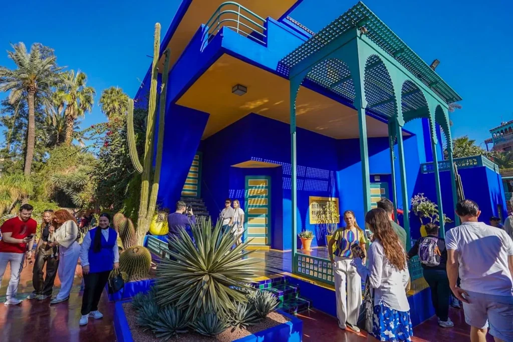 Visitors walking around the bright blue villa and exotic plants inside Majorelle Garden in Marrakech, Morocco, on a sunny day.
