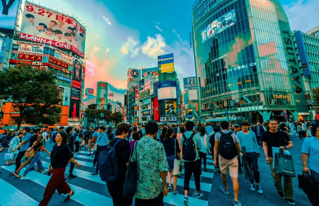Crowds crossing Shibuya Crossing in Tokyo surrounded by bright neon billboards and tall modern buildings during sunset. A famous landmark and must-visit spot for first-time travelers in Japan.