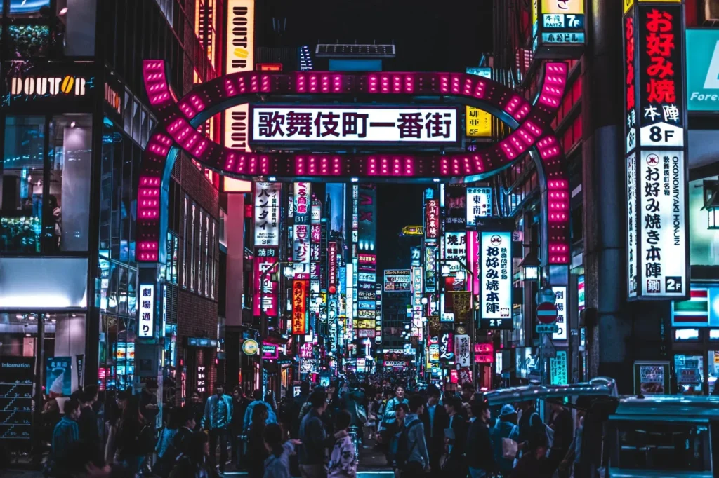 Kabukichō street in Tokyo illuminated by colorful neon signs with a crowd of pedestrians at night.